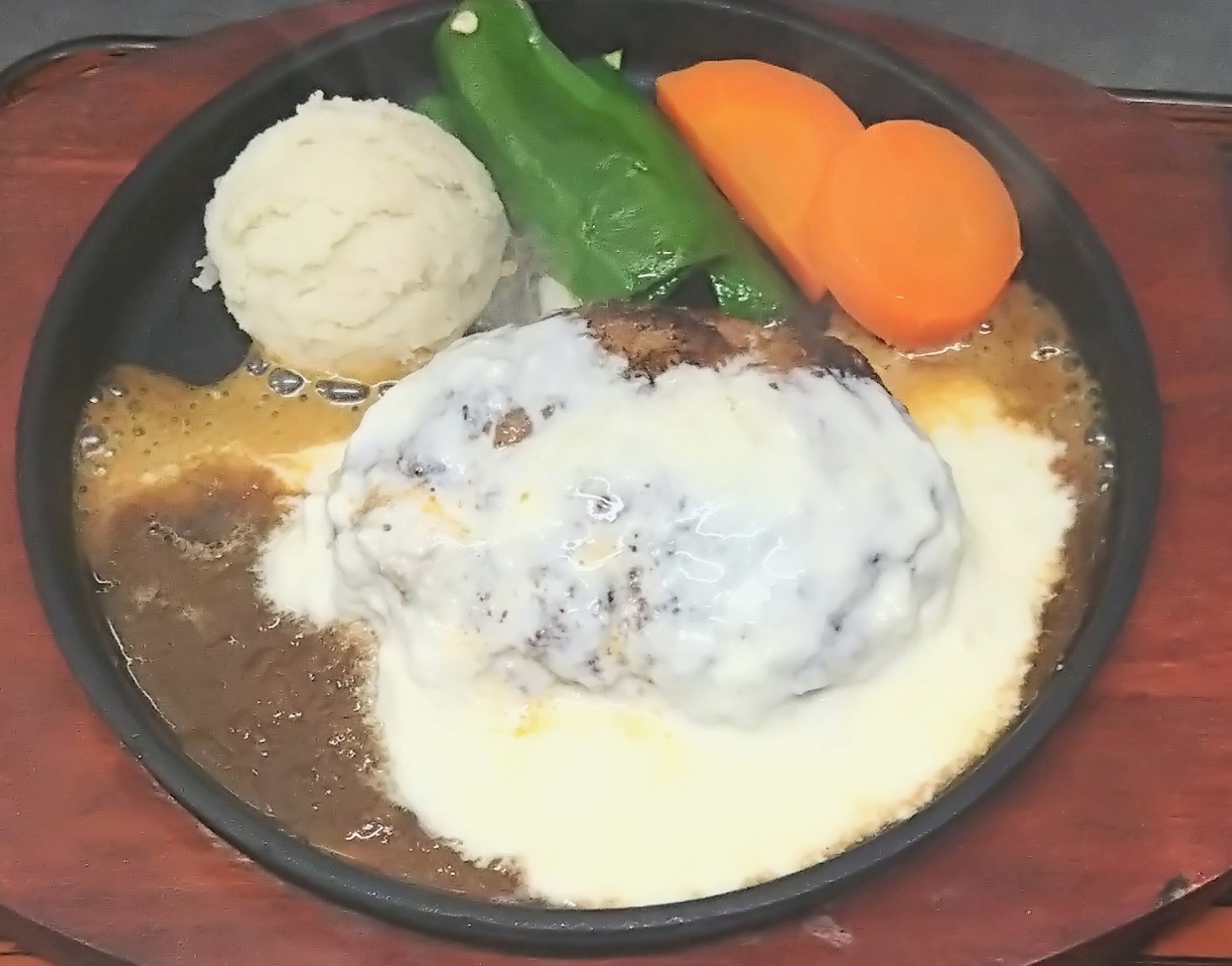 たっぷりのチーズソースが乗ったハンバーグ。付け合わせには人参とピーマン、マッシュポテトが乗っている。