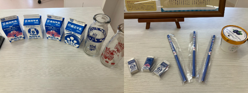 木目調のテーブル上に、酪王牛乳パック型の消しゴムやガラス瓶などのレトロ風グッズが並び、右側には同シリーズの消しゴムや青い鉛筆、丸い缶ケースが整然と配置されている。