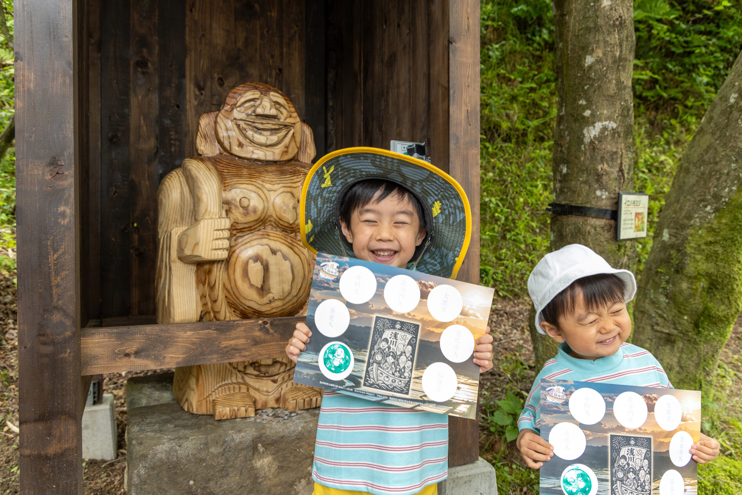「あさかわ七福神巡り」:二人の男の子が布袋尊像の前でスタンプラリーを楽しんでいる様子